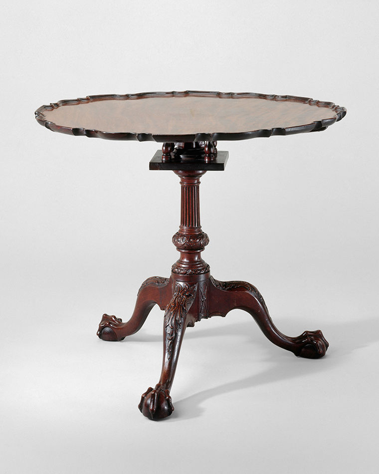 A round tea table with three legs jutting out and curling on the floor like large paws.